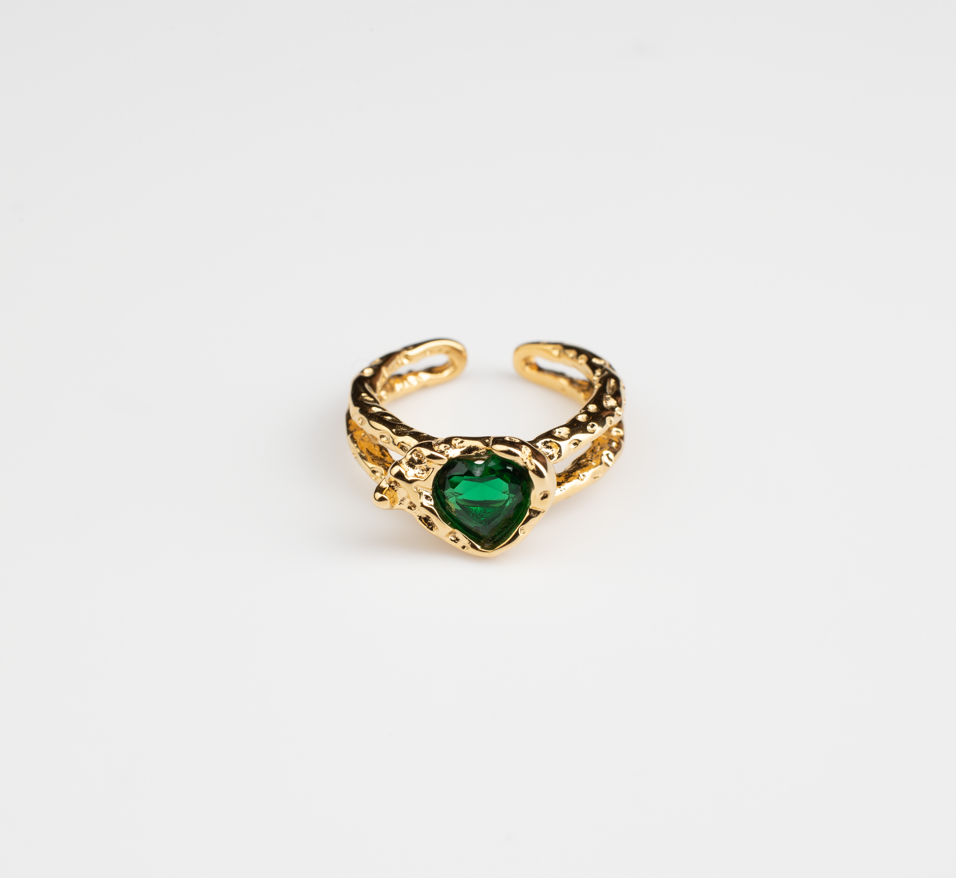 This is an open adjustable ring with a heart-shaped ring face, featuring a sparkling green gemstone embedded within the heart-shaped surface. The ring band, crafted from titanium steel plated with 18K gold, showcases an intricate hollow design and an open setting, suitable for hands of various sizes.