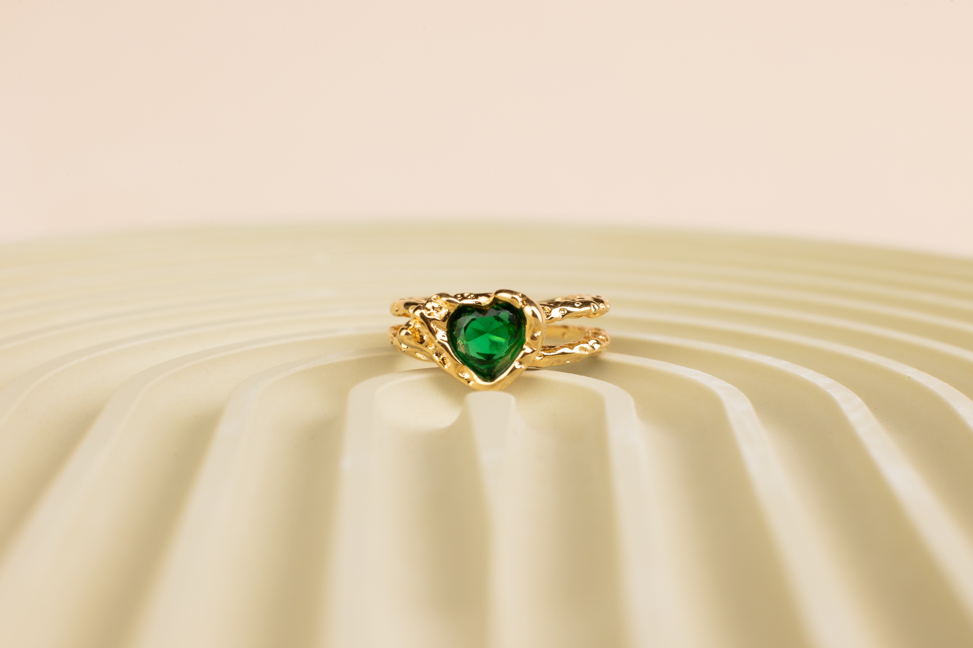 This is an open adjustable ring with a heart-shaped ring face, featuring a sparkling green gemstone embedded within the heart-shaped surface. The ring band, crafted from titanium steel plated with 18K gold, showcases an intricate hollow design and an open setting, suitable for hands of various sizes.