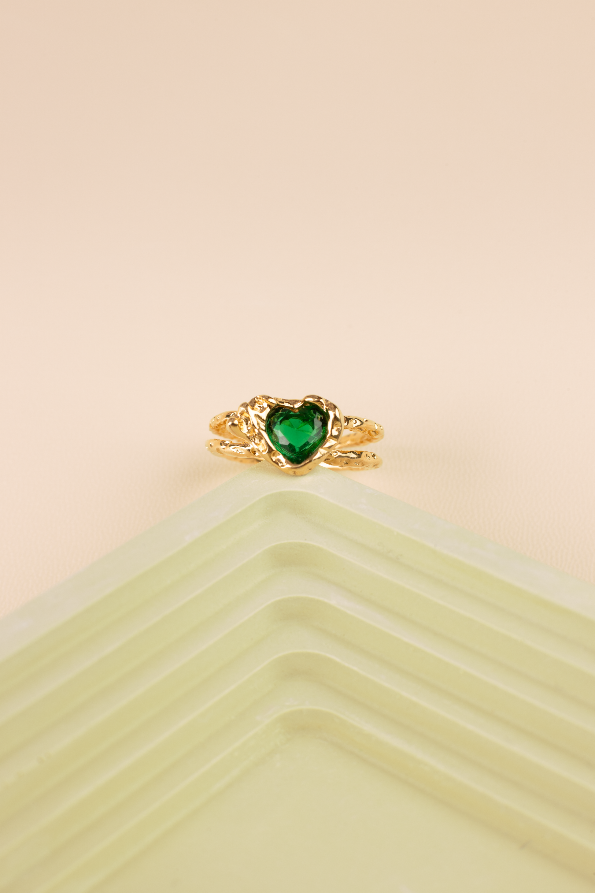 This is an open adjustable ring with a heart-shaped ring face, featuring a sparkling green gemstone embedded within the heart-shaped surface. The ring band, crafted from titanium steel plated with 18K gold, showcases an intricate hollow design and an open setting, suitable for hands of various sizes.