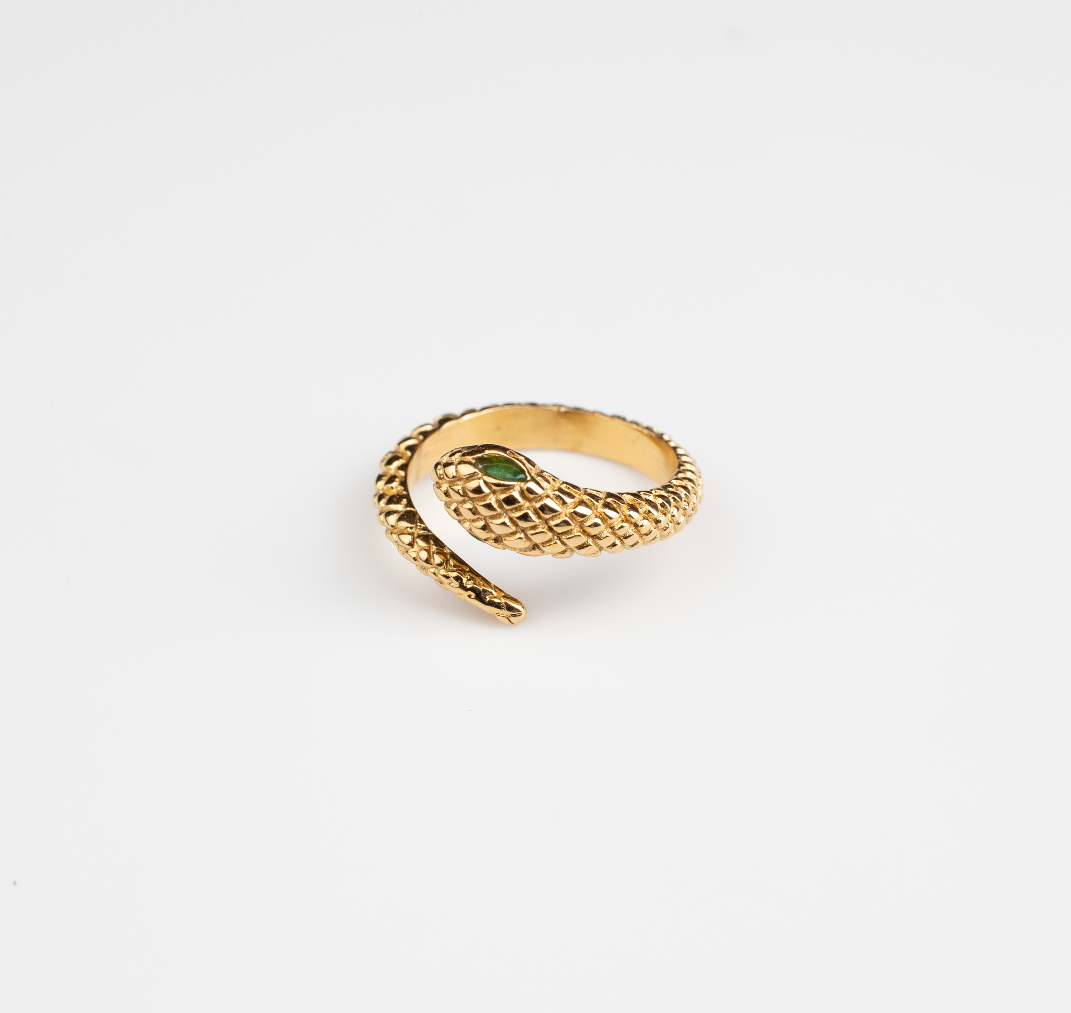 This ring features a snake motif, coiling around the finger with the opening positioned at the head where the snake's head meets its tail. The snake's head is adorned with a vibrant green gemstone, serving as its eyes. Lifelike scales cover the entire surface of the ring, available in both gold and silver options.