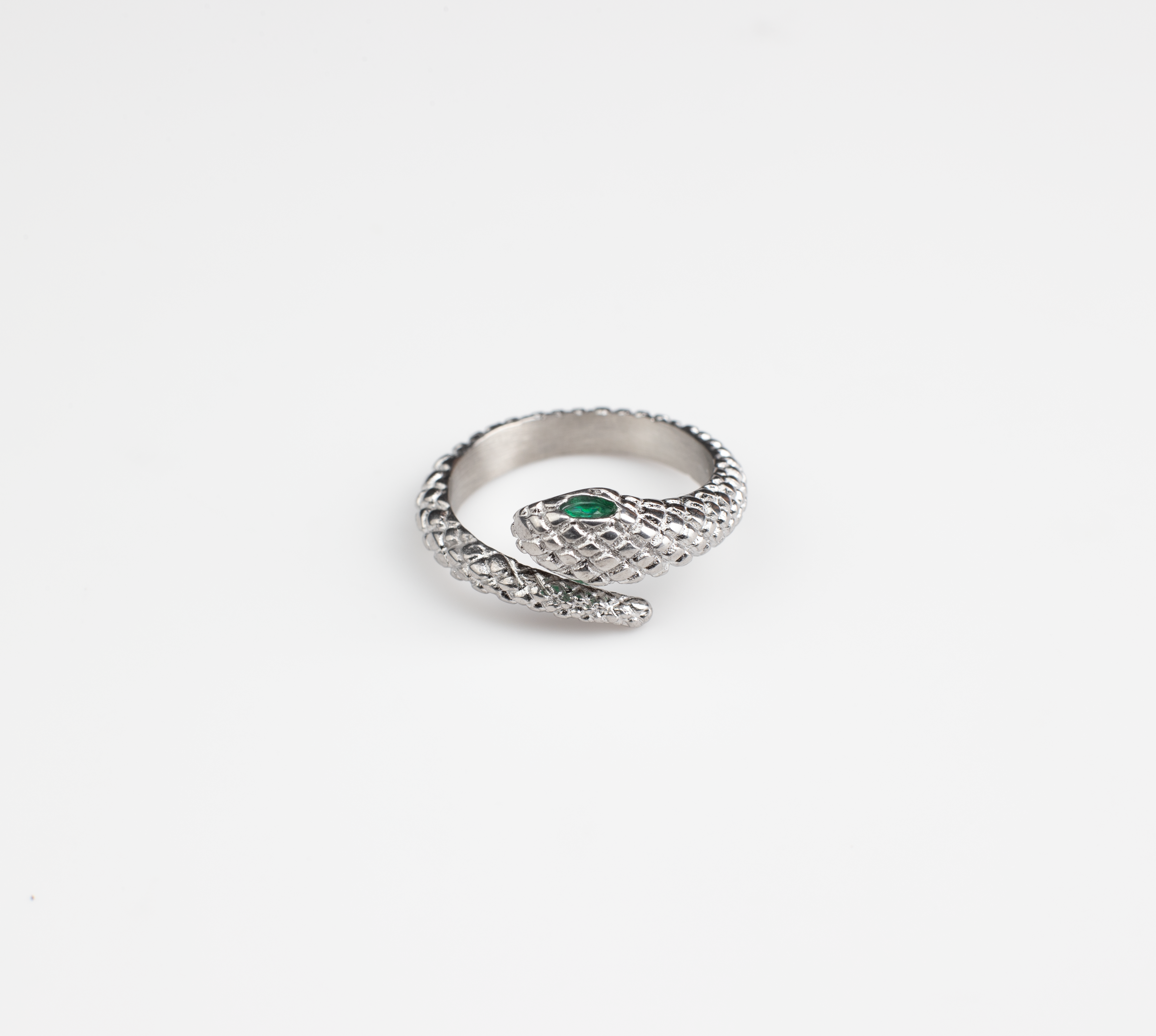 This ring features a snake motif, coiling around the finger with the opening positioned at the head where the snake's head meets its tail. The snake's head is adorned with a vibrant green gemstone, serving as its eyes. Lifelike scales cover the entire surface of the ring, available in both gold and silver options.