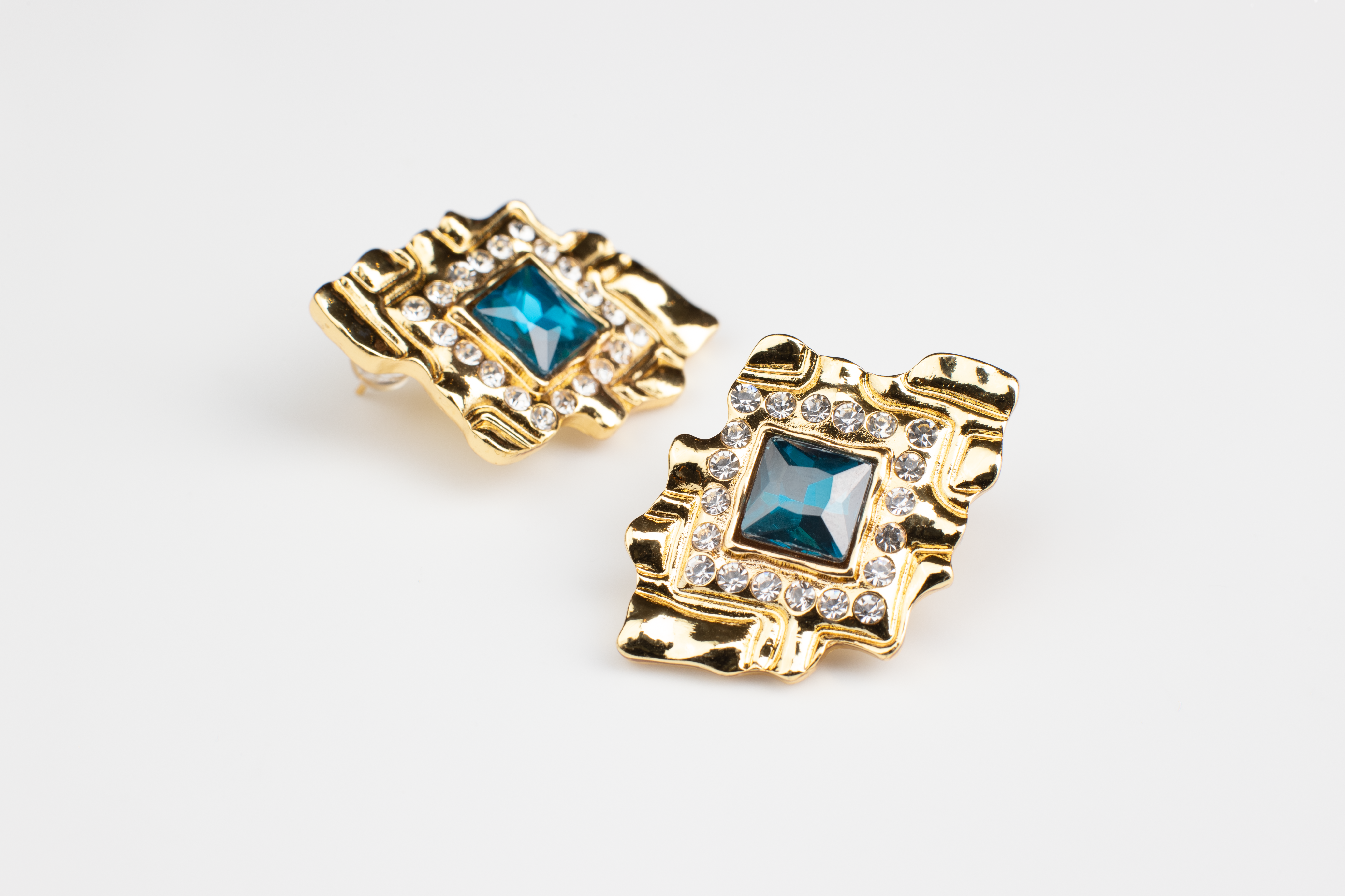 These diamond-shaped earrings feature a striking blue gemstone set within a golden frame adorned with sparkling diamond accents. Radiating luxury and elegance, they make a perfect accessory for women, suitable for various outfits and occasions. An ideal gift choice.