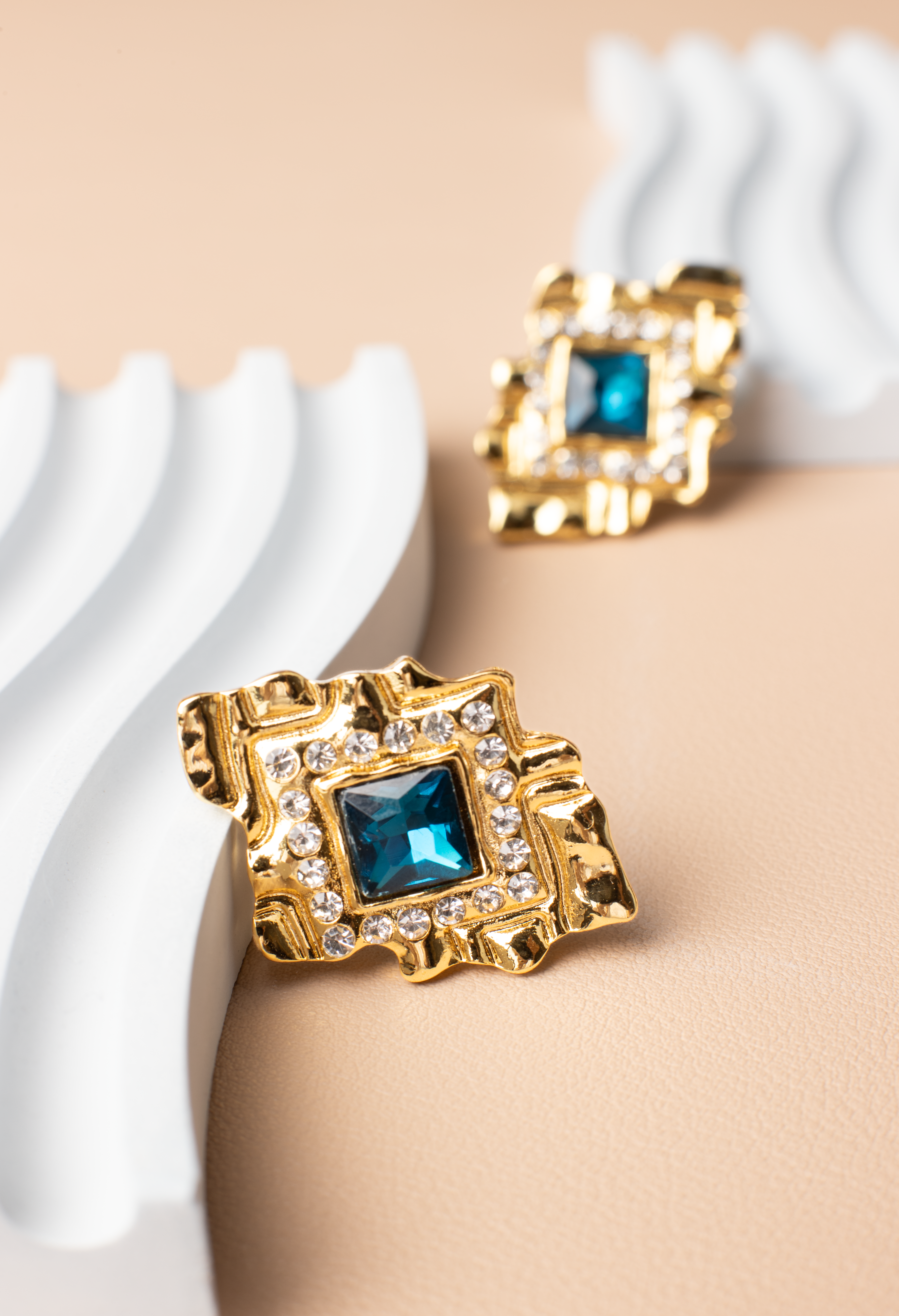 These diamond-shaped earrings feature a striking blue gemstone set within a golden frame adorned with sparkling diamond accents. Radiating luxury and elegance, they make a perfect accessory for women, suitable for various outfits and occasions. An ideal gift choice.