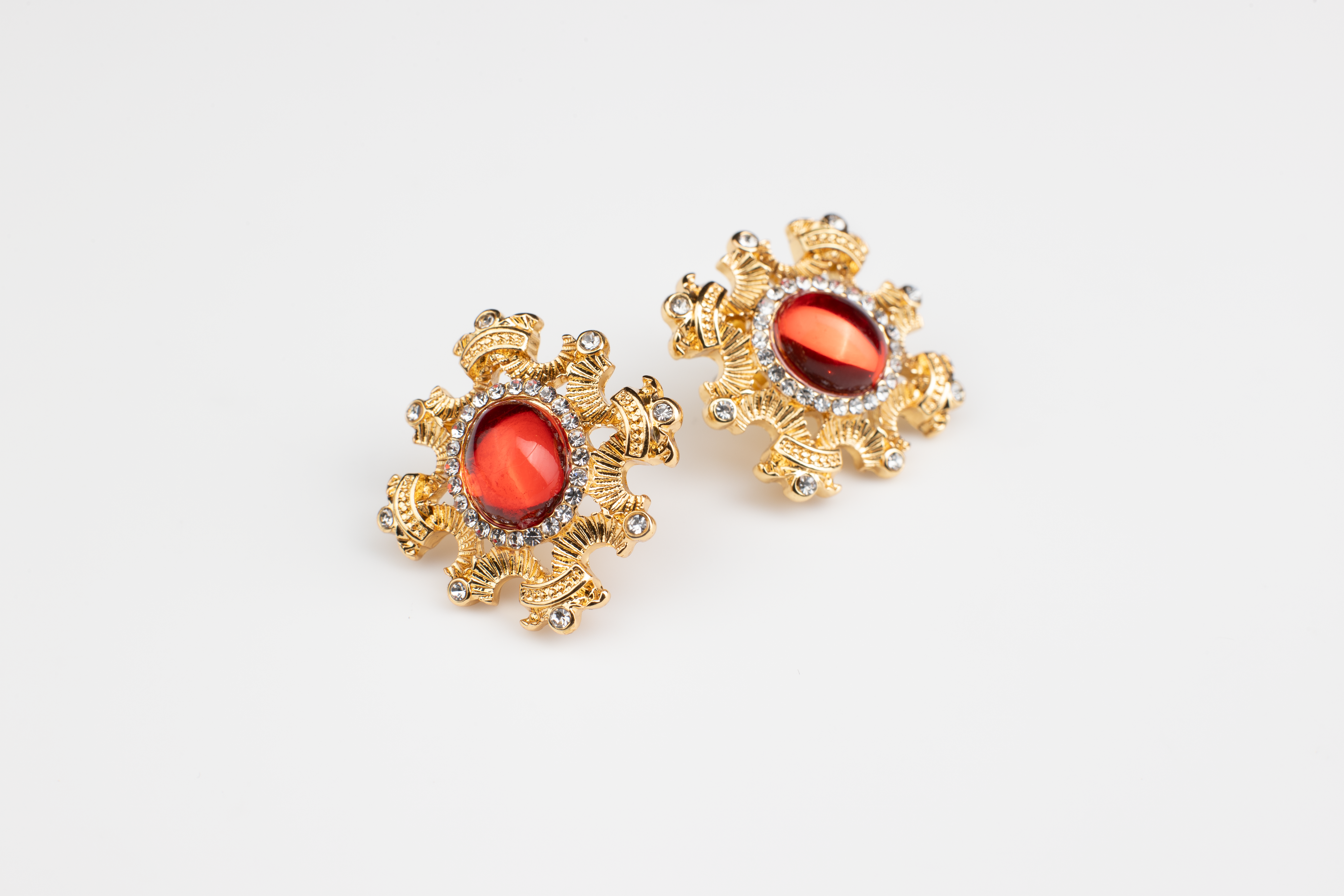 Adorn yourself with the regal elegance of red gemstone earrings encased in a blossoming gold frame. This bold and fiery design is suitable for various occasions, with the option of ear clips for added versatility. A perfect gift choice."