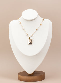 Book-shaped locket necklace with a celestial design featuring stars, a crescent moon, and sparkling gemstone accents. Made from copper with 14K gold plating, this openable locket is elegantly displayed on a white velvet bust stand with a wooden base, perfect for showcasing its timeless charm and photo-holding functionality.