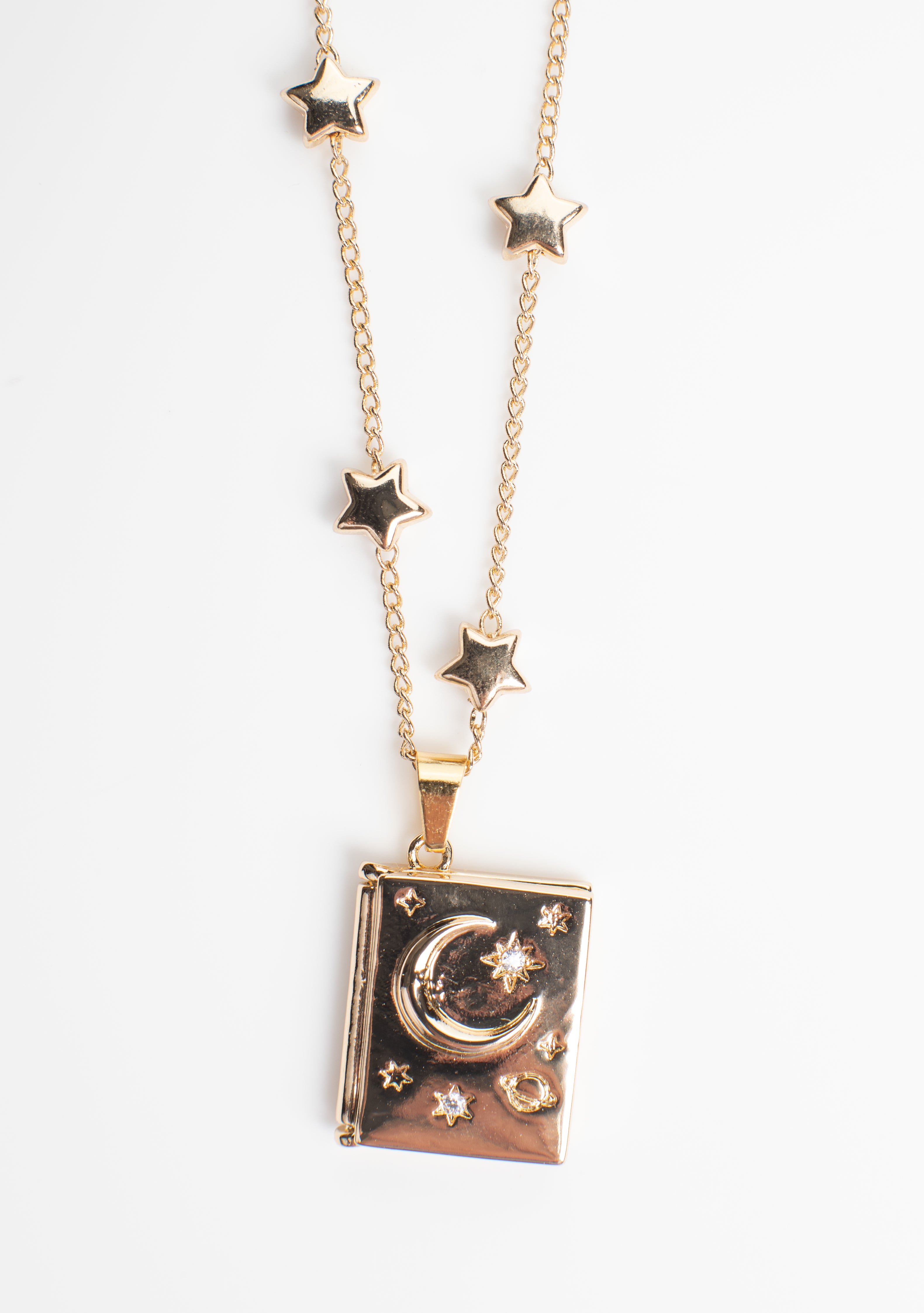 Book-shaped locket necklace with a celestial design featuring stars, a crescent moon, and sparkling gemstone accents. Crafted from copper with 14K gold plating, this locket opens from the side to reveal a hidden photo compartment, elegantly displayed against a clean white background.